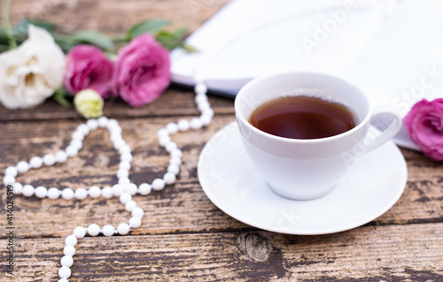 Morning time, beautiful picture for blog post in Instagram. Relax and have cup of coffee or tea with book, decorated by flowers and beads as heart. Enjoy your free minutes. Wooden background