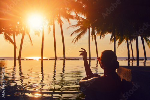 Vacation Beach Summer Holiday Concept. Silhouette woman relaxing in swimming pool on summer beach resort watching sunset.