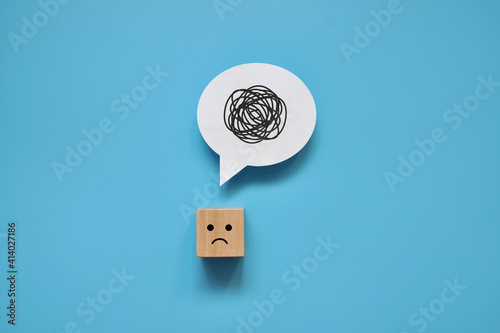 A wooden cube with a sad face with a tangle of thoughts in its head.  photo