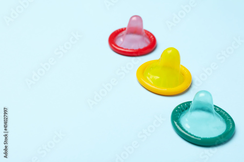 Multicolored condoms on blue background, space for text