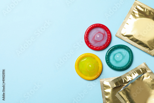 Multicolored condoms on blue background, space for text