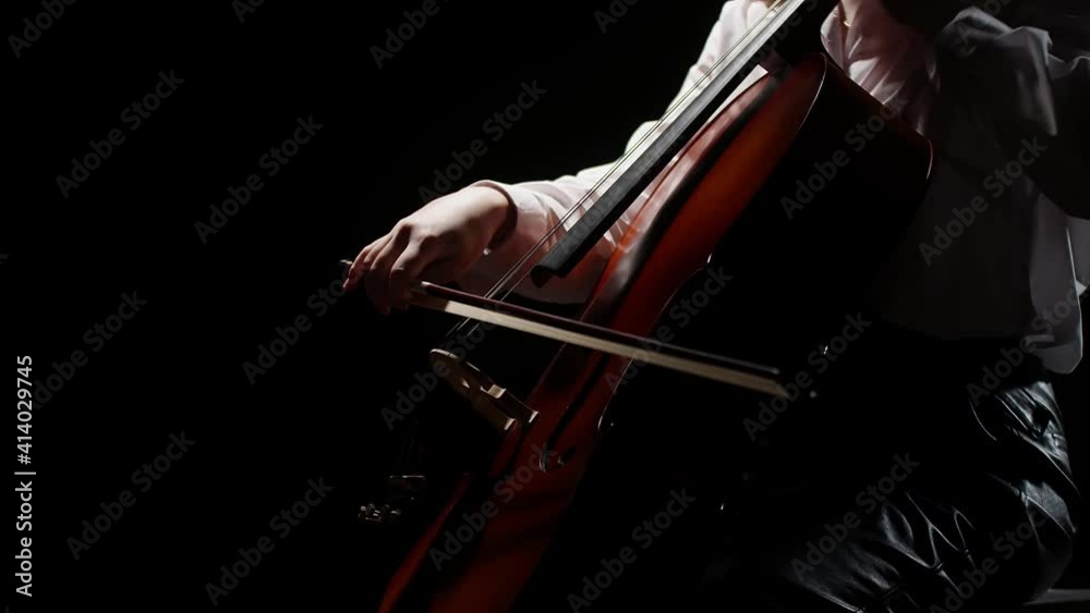 Musician plays with his hand using a bow on the strings of the cello in the darkness. Close-up artist plays on the violoncello.