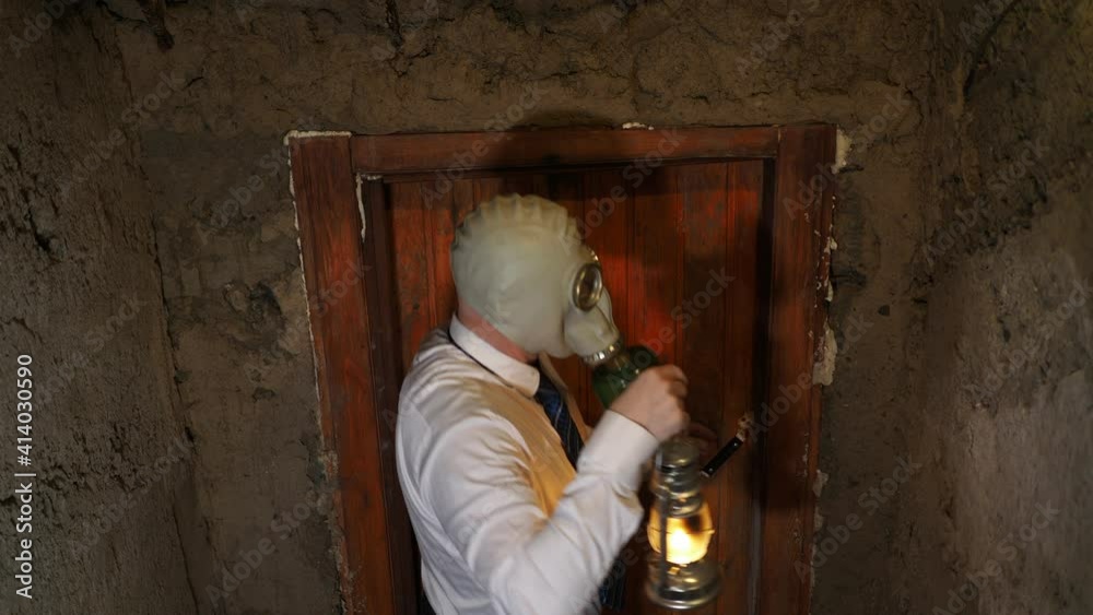 Post-apocalypse, Covid-19. A man in a gas mask during an epidemic descends into a concrete bunker with a kerosene lamp in his hand.