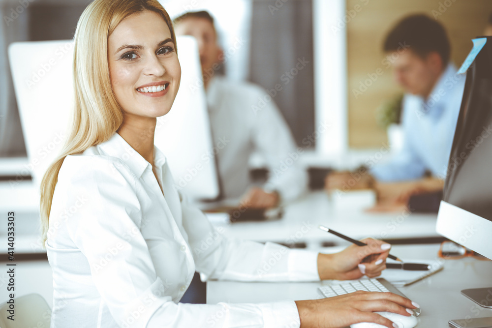 Obraz premium Business woman using computer at workplace in modern office. Secretary or female lawyer smiling and looks happy. Working for pleasure and success