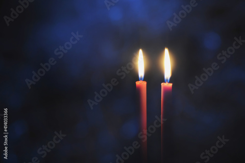 Burning candles in Darkness. Two red candles on black background with blue light bokeh.