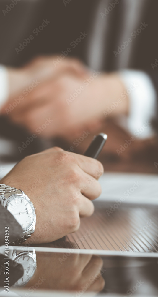 Obraz premium Unknown businessman shaking hands with his colleague or partner above the glass desk in modern office, close-up. Business people group at meeting