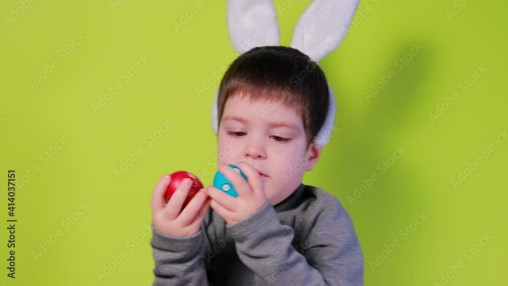 Cheerful happy boy with bunny ears on head is playing with Easter colorful eggs, beating painted chicken eggs against each other. Easter kid on a yellow background. Cheerful happy boy with bunny ears on head is playing with Easter colorful eggs, beating painted chicken eggs against each other. Easter kid on a yellow background.