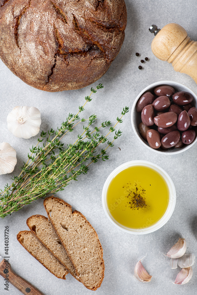 Fototapeta premium Bread, olive oil, kalamata olives, garlic and herbs on blue background, view from above