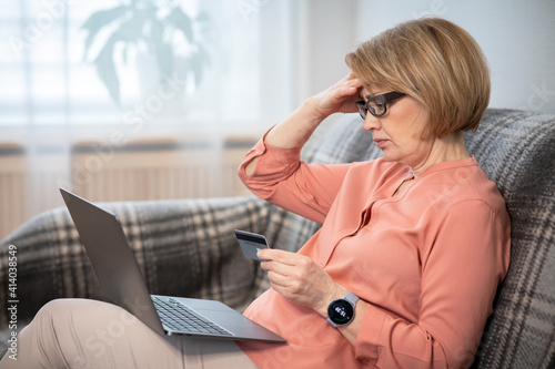 Nervous horrified confused elderly senior retired woman, stressed worried sad frustrated lady having problem with paying, buying online, payments with credit blocked bank card, laptop. Internet fraud