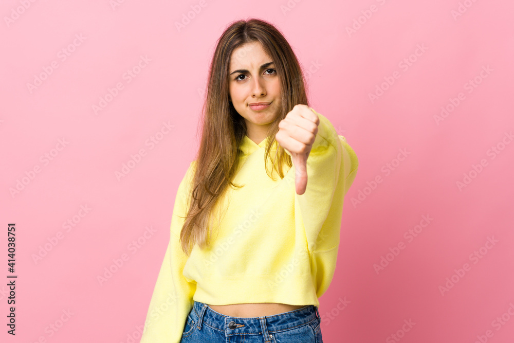 Young woman over isolated pink background showing thumb down with negative expression Young woman over isolated pink background showing thumb down with negative expression