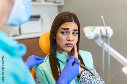 Fotografie Young woman holding cheek in chair at dentist, having toothache