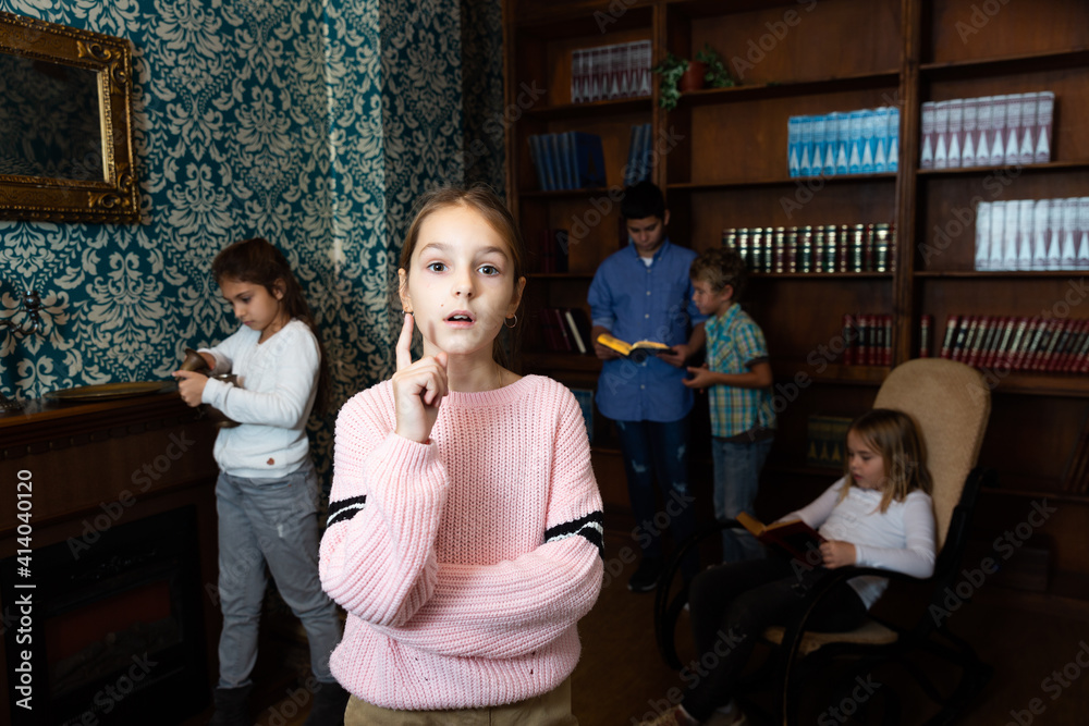 Portrait of pensive tween girl solving riddles in quest room, pointing with her forefinger. Concept of found solution