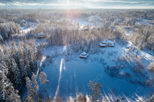 Wooden cabins captured from birds eye view, deep winter snow during sunny morning.