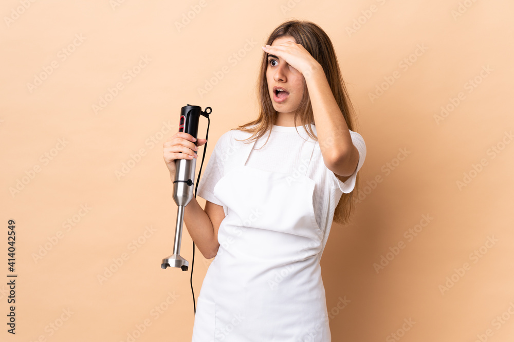 Woman using hand blender over isolated background with surprise expression while looking side Woman using hand blender over isolated background with surprise expression while looking side