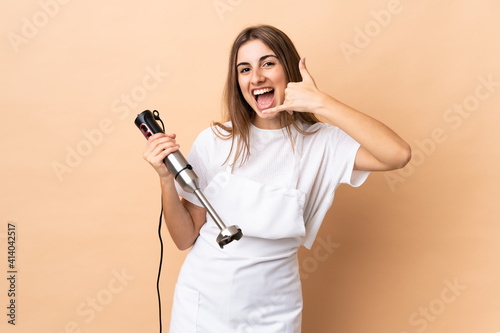 Woman using hand blender over isolated background making phone gesture. Call me back sign