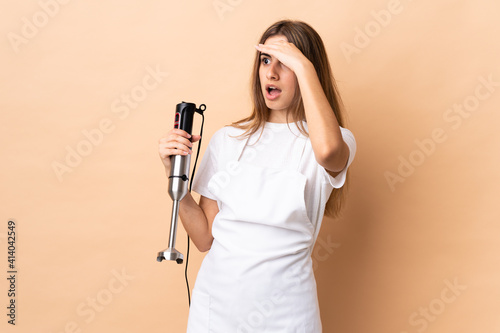 Woman using hand blender over isolated background with surprise expression while looking side