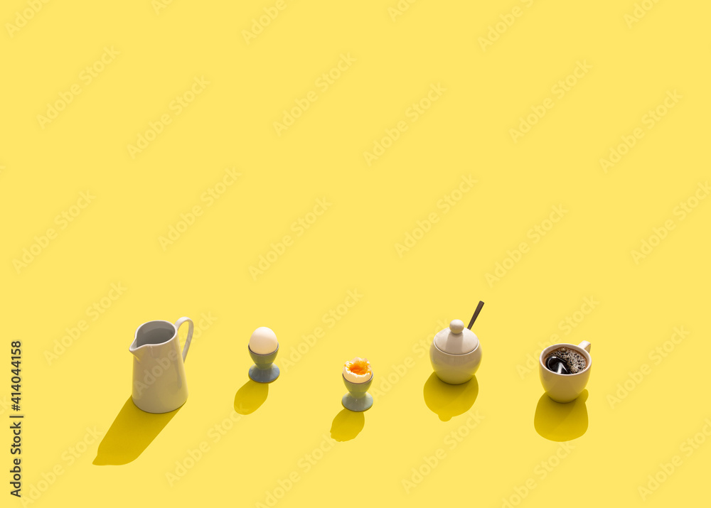 Breakfast set with soft boiled eggs, black coffee in white cup, milk jug, sugar bowl. Hard light, yellow bright background. Hard shadows breakfast, simple minimal concept. Template, space for text