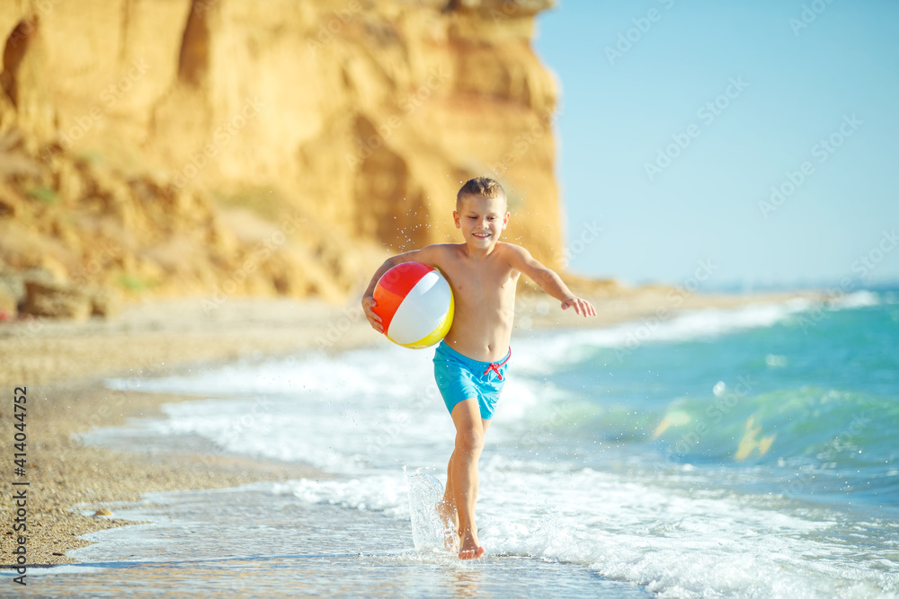 Boy child has fun at sea. Summer, happiness, sea and a child with a ball. High quality photo.