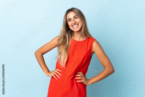 Young hispanic woman over isolated blue background posing with arms at hip and smiling