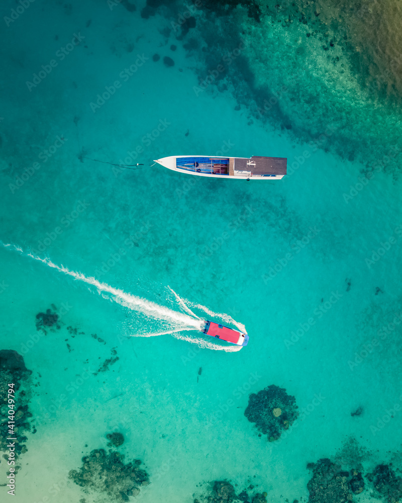 Aerial view of two fishing boats sailing in the blue water along Maratua Island shoreline, Kalimantan Timur, Indonesia. Aerial view of two fishing boats sailing in the blue water along Maratua Island shoreline, Kalimantan Timur, Indonesia.