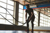 Muscular man in the gym with ropes doing exercises. Crossfit Silhouette photography
