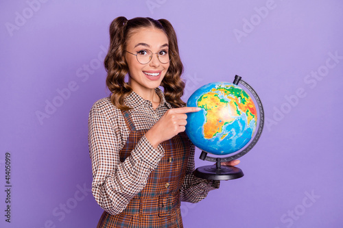 Portrait of half turned pretty girl arms hold globe direct finger continent isolated on purple color background