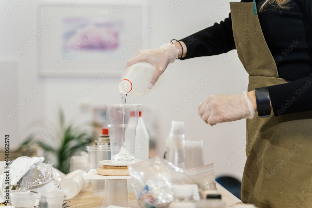 a girl in an apron and transparent gloves pours clear liquid from a white plastic bottle into a transparent plastic cup a girl in an apron and transparent gloves pours clear liquid from a white plastic bottle into a transparent plastic cup