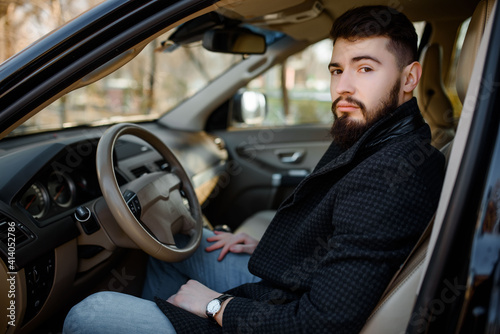 bearded stylish young handsome man in black coat sitting in the car