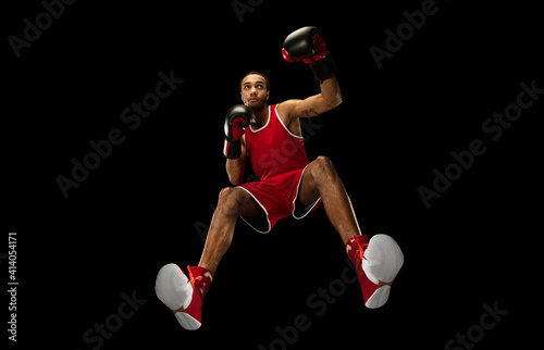 Young african-american professional boxer in action, motion isolated on black background, look from the bottom. Concept of sport, movement, energy and dynamic, healthy lifestyle. Training, practicing.