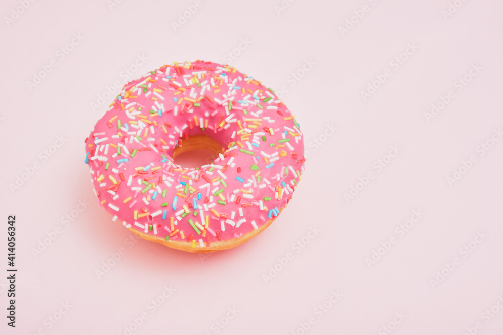Donut with pink icing and pastry sprinkles on a pink background