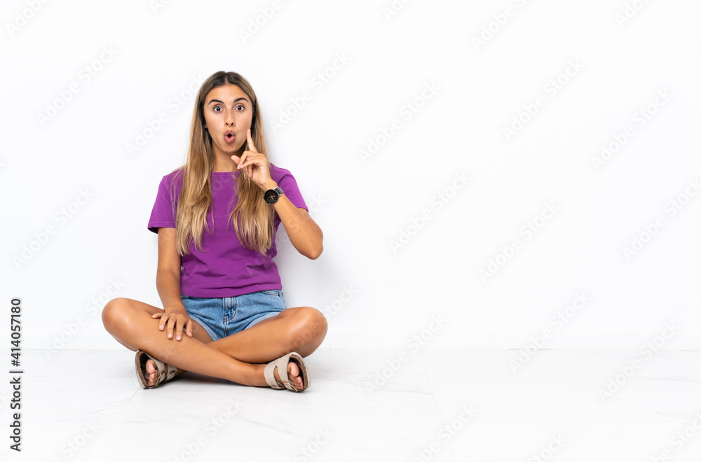 Young hispanic woman sitting on the floor intending to realizes the solution while lifting a finger up