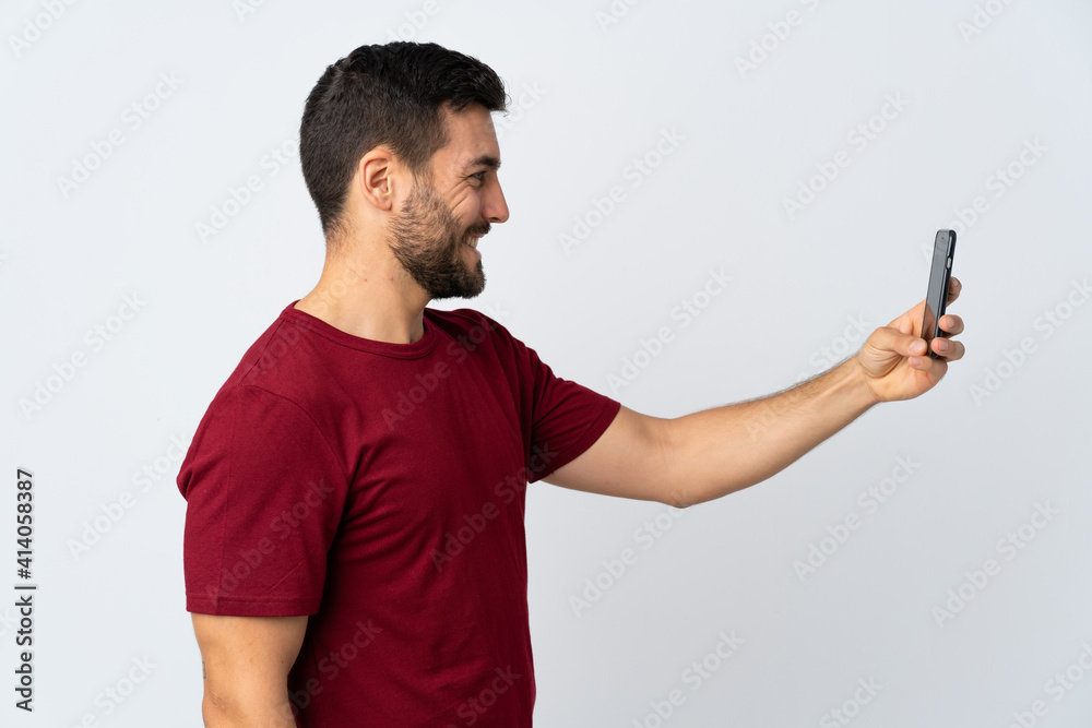 Young handsome man with beard using mobile phone isolated on white background with happy expression Young handsome man with beard using mobile phone isolated on white background with happy expression