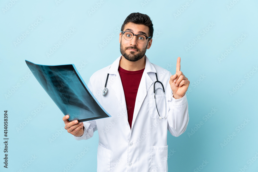 Professional traumatologist holding radiography isolated on blue background pointing with the index finger a great idea