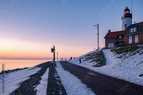 Winter in Urk with the dike and beach by the lighthouse of Urk snow covered during winter, sunset by the lighthouse of Urk Flevoland. Netherands photo