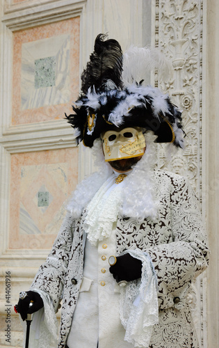 Mask in  in traditional Venetian costume perfectly compatible with palazzo wall at background at traditional Carnival in Vemice, Italy. 