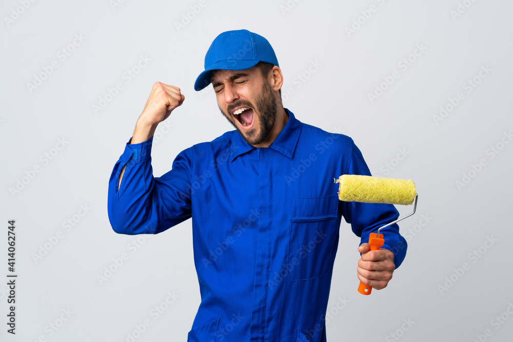 Painter man holding a paint roller isolated on white background celebrating a victory Painter man holding a paint roller isolated on white background celebrating a victory