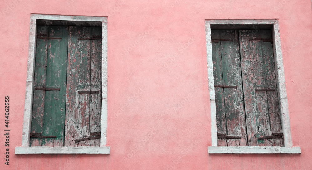 Abandoned palazzo in Venice, Italy. Pink stucco wall and closed wooden shutters with peeling paint.