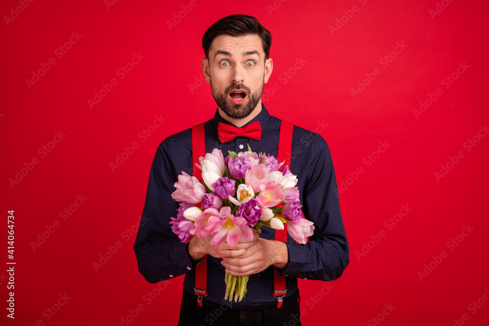 Photo of young handsome amazed surprised man hold bouquet receive birthday present isolated on red color background Photo of young handsome amazed surprised man hold bouquet receive birthday present isolated on red color background
