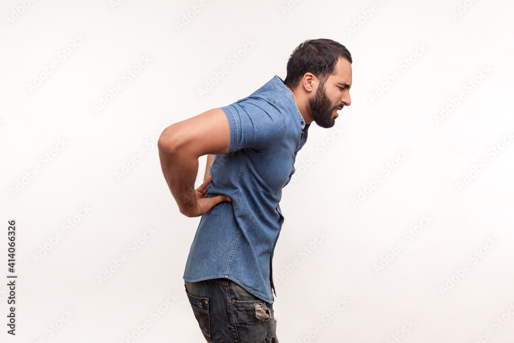 Side view exhausted unhealthy bearded man touching aching back, suffering lower lumbar discomfort, muscle pain, injured spine disk. Indoor studio shot isolated on white background Side view exhausted unhealthy bearded man touching aching back, suffering lower lumbar discomfort, muscle pain, injured spine disk. Indoor studio shot isolated on white background