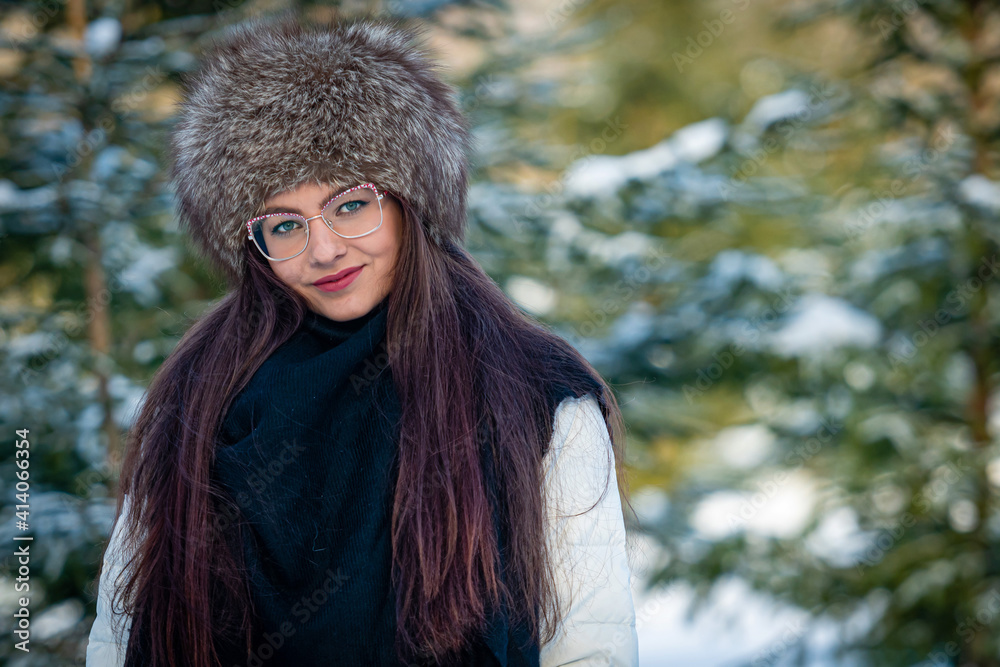 cheerful lady in glasses and winter clothes posing with joy outside in the snow forest