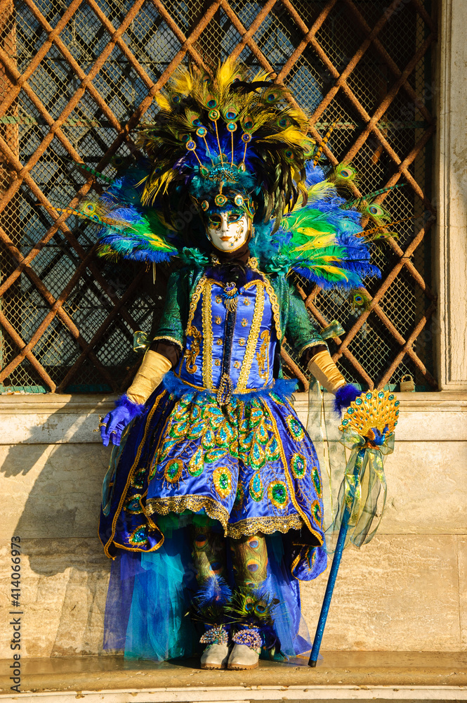 Peacock mask in sunlight near Doge's Palace in St Mark's Square at traditional Carnival in Venice, Italy. 