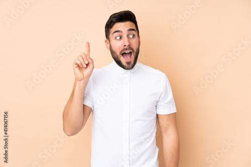 Caucasian handsome man isolated on beige background intending to realizes the solution while lifting a finger up