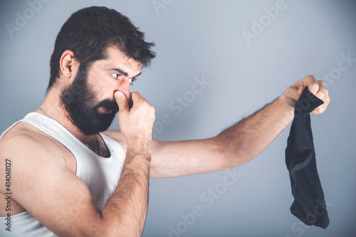A young man holds his smelly socks and covers his nose with his hand. Nasty smell. Stink legs, fungus on the legs.