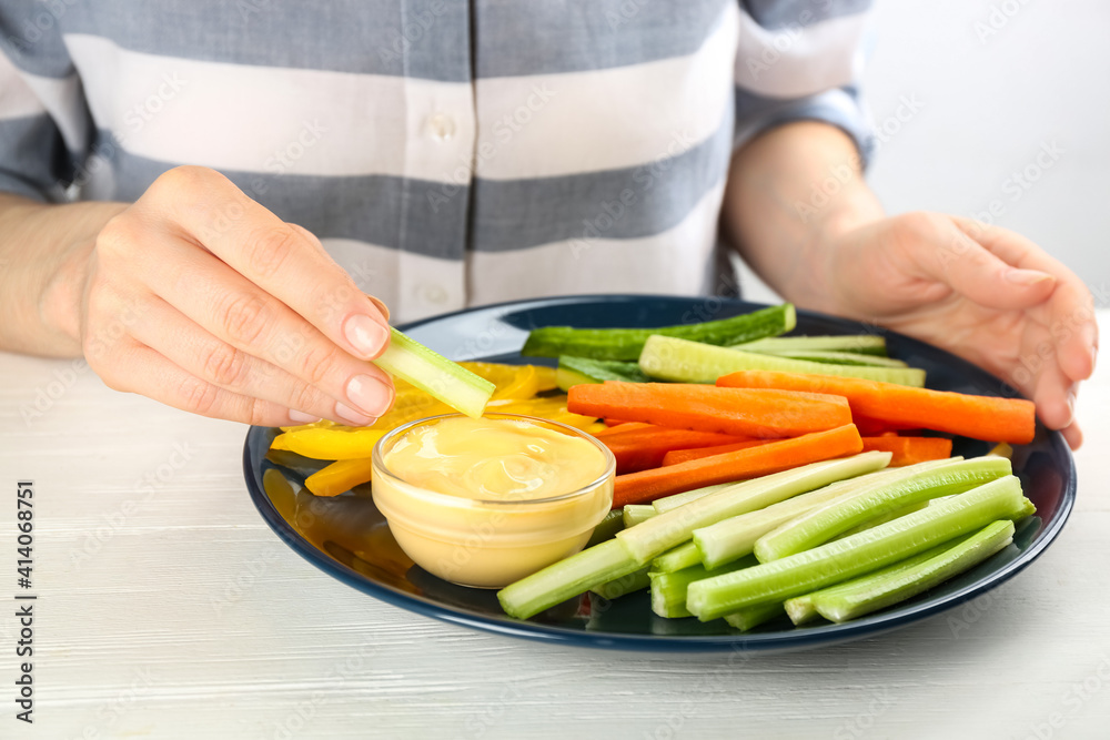 Woman dipping celery stick in sauce at white wooden table, closeup Woman dipping celery stick in sauce at white wooden table, closeup