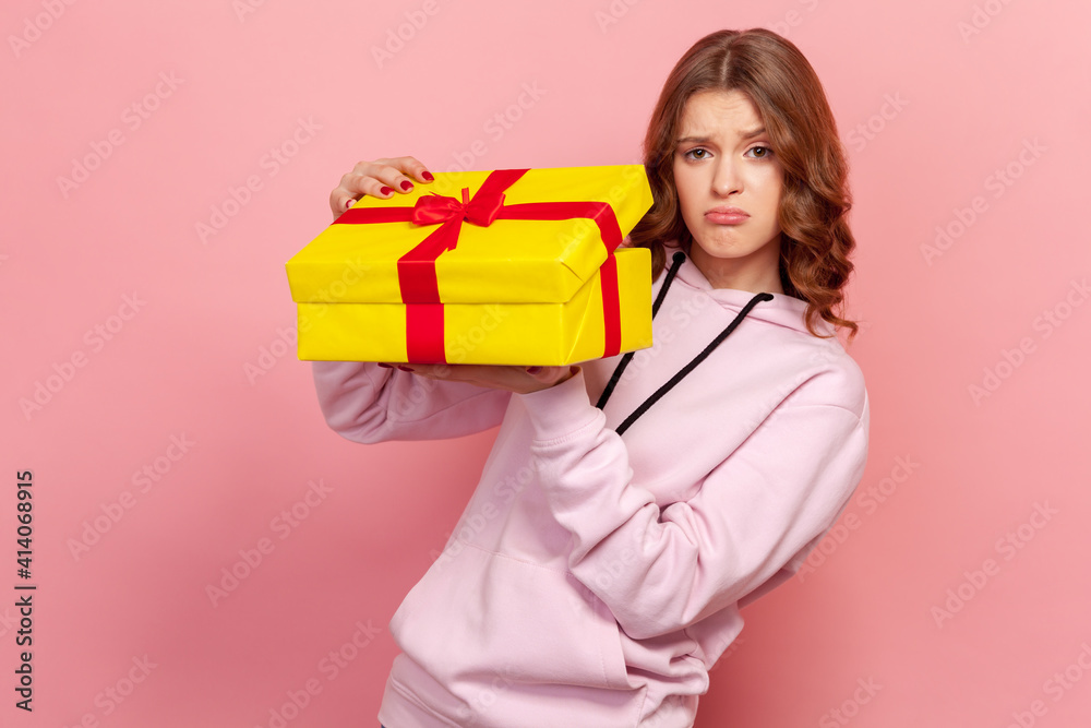 Portrait of displeased teenage girl in hoodie opening birthday gift on party celebration, looking disappointed unhappy. Indoor studio shot isolated on pink background Portrait of displeased teenage girl in hoodie opening birthday gift on party celebration, looking disappointed unhappy. Indoor studio shot isolated on pink background