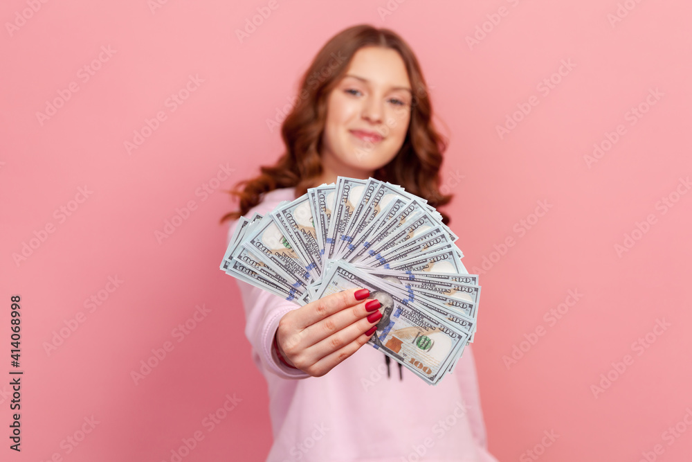 Portrait of satisfied curly haired young female lottery winner showing bunch of dollar banknotes at camera, profit and finance. Indoor studio shot isolated on pink background Portrait of satisfied curly haired young female lottery winner showing bunch of dollar banknotes at camera, profit and finance. Indoor studio shot isolated on pink background
