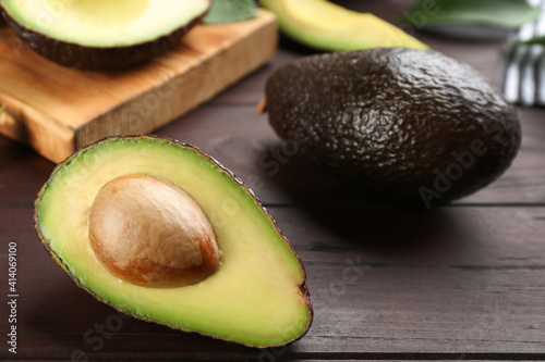 Whole and cut avocados on wooden table, closeup