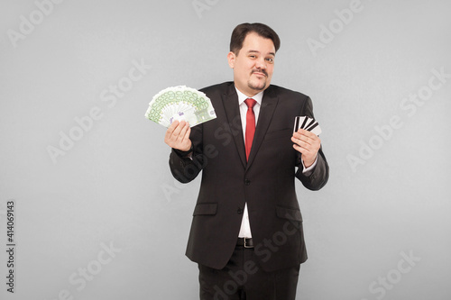 Businessman can not choose, online banking or money on his hands. Indoor, studio shot, isolated on gray background photo