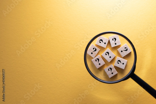 Focus on Question Mark symbol on a wooden tiles using magnifying glass against yellow background. Concept of Q and A, questions and faq