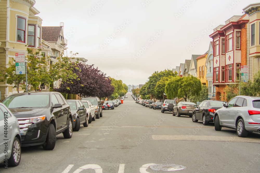 Horizontal shot of a beautiful street with trees, parked cars and classic San Francisco houses on both sides, California - United States of America aka USA